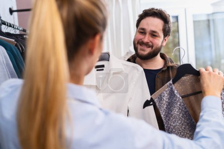 Saleswoman presenting a shirt to a male customer who is examining a patterned jacket at a store