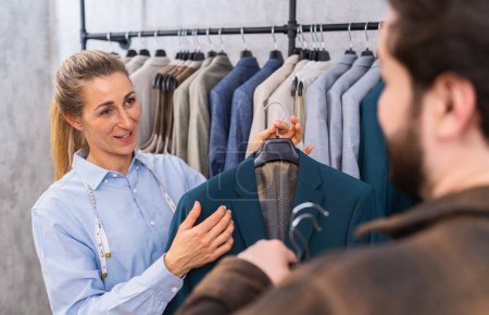 Tailor holding a teal jacket for a male client, both engaging in conversation at a store