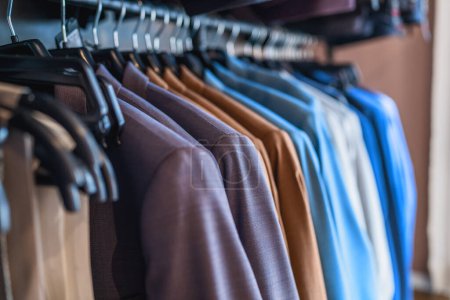 Reihe verschiedenfarbiger Anzüge auf Kleiderbügeln in einem Bekleidungsgeschäft
