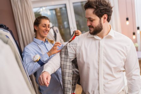 Téléchargez les photos : Tailleur mesurant une veste sur un client dans un magasin de costumes - en image libre de droit