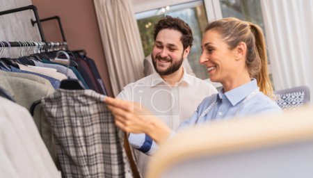 Sastre y cliente seleccionando una chaqueta de traje de un estante en una boutique de bodas