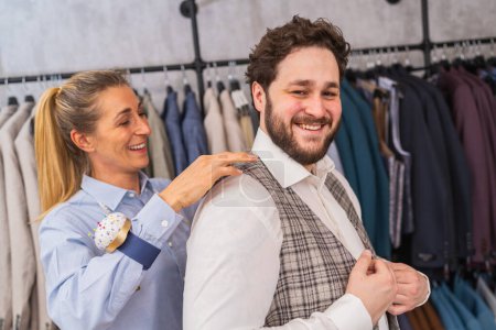Tailor fitting a vest on a cheerful male client in a clothing store