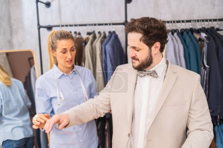 Tailor examining sleeve length on a man's suit in a clothing shop with a concerned expression