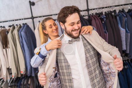 Tailor helping a man try on a jacket in a boutique, both are smiling
