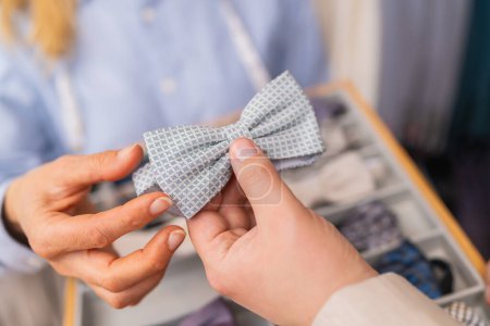 Close-up of hands holding a light blue patterned bow tie in a tailor shop
