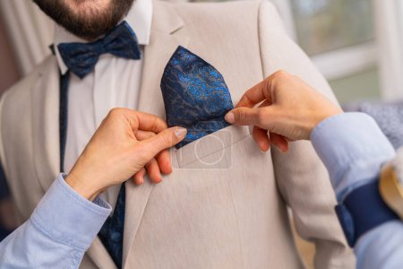 Close-up of tailor placing a blue patterned pocket square in a suit jacket