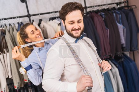 Tailor playfully pulling on client's suspenders, cheerful atmosphere in suit shop