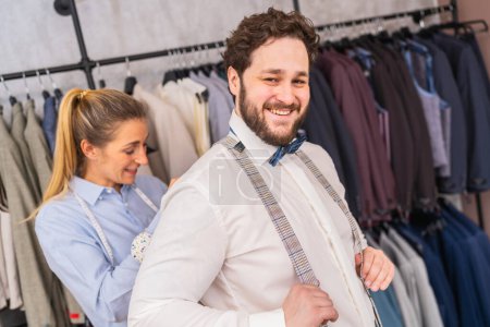 Tailor fastening suspenders for a smiling man in a clothing boutique