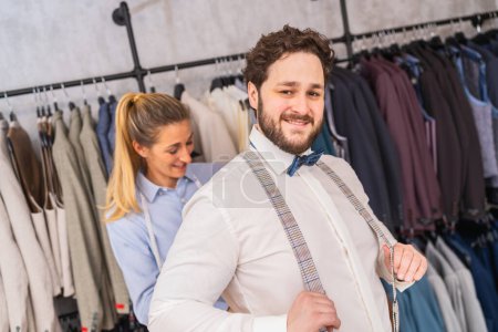 Tailor fastening a happy man's suspenders in a bright clothing store