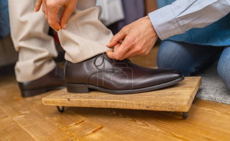 Le tailleur ajuste la longueur du pantalon d'un homme sur une chaussure brune sur un repose-pieds en bois
