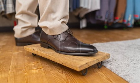 Man trying on brown leather shoes, standing on one foot on a wooden board