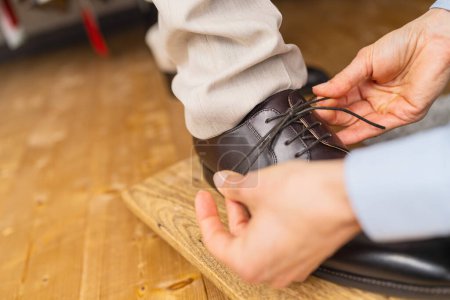 Gros plan des mains attachant les lacets d'une nouvelle chaussure en cuir marron sur une planche en bois dans un magasin de mariage
