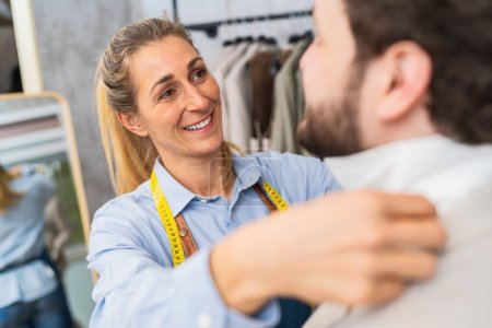 Téléchargez les photos : Femme sur mesure portant une chemise sur un client masculin, souriant tous les deux dans un magasin - en image libre de droit