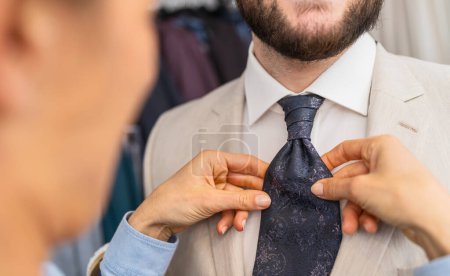 Saleswoman adjusting a tie on a man in a beige suit
