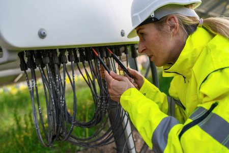 Technician checking solar panel cables with a multimeter in a solarpark field. Alternative energy ecological concept image.