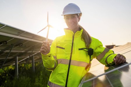 Technicien en énergie renouvelable tenant un modèle d'éolienne au parc solaire. Image concept écologique énergie alternative.