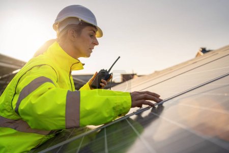 Téléchargez les photos : Technicien solaire avec talkie-walkie inspectant les panneaux solaires au crépuscule. Image concept écologique énergie alternative. - en image libre de droit