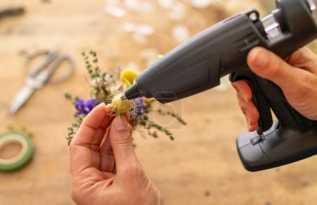 Téléchargez les photos : Mains en utilisant un pistolet à colle sur un petit projet d'artisanat floral - en image libre de droit
