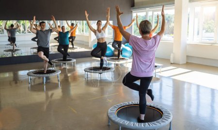 Téléchargez les photos : Amateurs de fitness participant à un cours d'entraînement de trampoline dans une salle de gym ensoleillée - en image libre de droit
