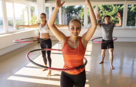 Photo for Young women an men doing hula hoop during an exercise class in a gym. Healthy sports lifestyle, Fitness, Healthy concept. - Royalty Free Image