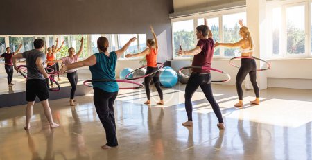 Photo for Team Sport Sporty women and men exercising with Hula hoop in fitness gym for healthy lifestyle concept. - Royalty Free Image