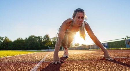 Foto de Deportista femenina determinada en posición inicial en pista de atletismo - Imagen libre de derechos