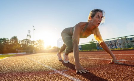 Photo for Female athlete in starting position on a track field during sunset - Royalty Free Image
