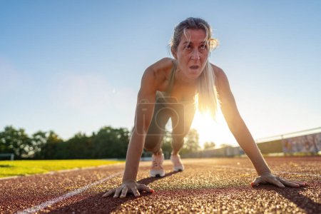 Photo for Intense female athlete at starting line on race track during sunset - Royalty Free Image