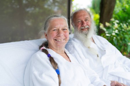 Happy similing senior couple relaxing together on bed lounge at wellness spa resort in the garden. Senior Moments concept image