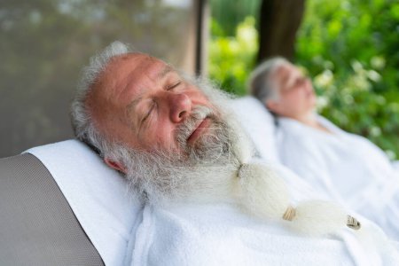 Seniorenpaar entspannt sich im Wellness-Kurort. Schöner alter Mann und attraktive alte Frau genießen die gemeinsame Zeit im Liegestuhl im Garten.