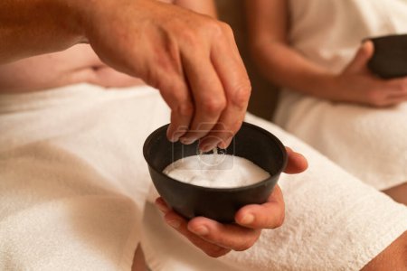 Man holds a bowl of salt in his hand at the steam bath or hammam to exfoliate the skin for body massage in a spa or wellness resort 