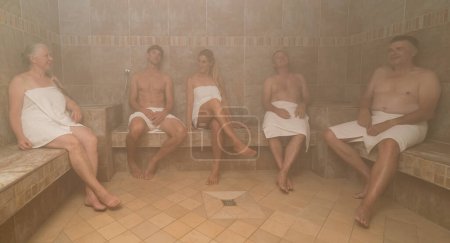 Eine Gruppe Erwachsener, in weiße Handtücher gehüllt, entspannt sich in einem tutkischen Dampfbad. Wellness- und Kurkonzeption Image