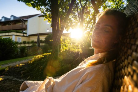 Zufriedene Frau entspannt sich auf einer Schaukel im Sonnenlicht, Augen zu und durch in einem Kurort