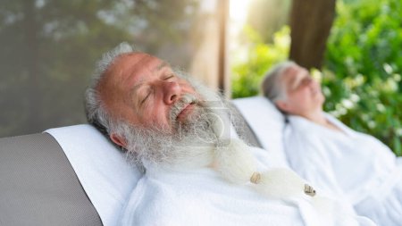 Älteres Paar entspannt sich in weißen Bademänteln auf Liegestühlen im Freien in einem Wellness-Hotel