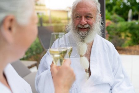 Älterer Mann mit weißem Bart lächelt und stößt mit einem Glas Champagner an