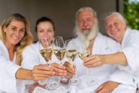 cuatro personas en albornoces blancos brindando con copas de champán y celebrando un día de spa en un hotel
