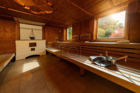 Finnische Sauna mit Fliesenboden, Holzbänken, Herd, Handtuch, Metalleimer, Schöpfkelle und Filzhüten mit Fenster mit Aussicht in einem Wellnesshotel
