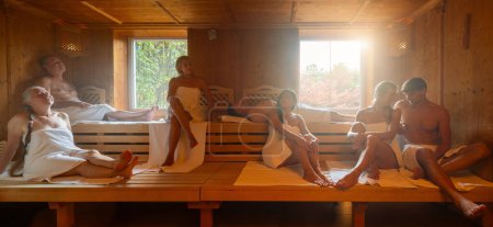 Grupo de personas de varias edades que se relajan juntos en la sauna finlandesa caliente. luz dramática con el concepto de vapor, spa y bienestar.