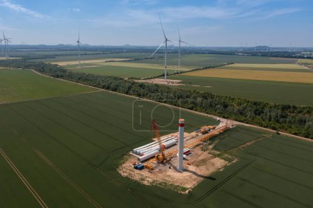 Wide aerial view of a wind turbine under construction in the midst of green fields