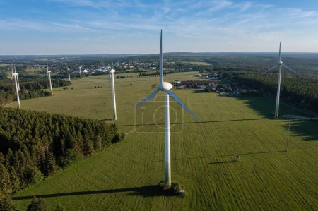 Aerial shot of wind turbines in a field next to a forest with a village in the distance. Renewable energy concept image