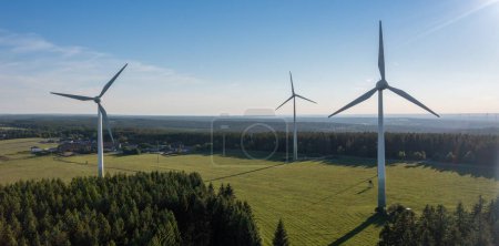 Wind turbines in a rural setting with forest in the background under a clear sky. Renewable energy concept image