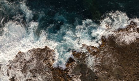 Foto de Vista aérea de las turbulentas olas marinas que se encuentran con la costa rocosa creando espuma en la isla fuerteventura - Imagen libre de derechos