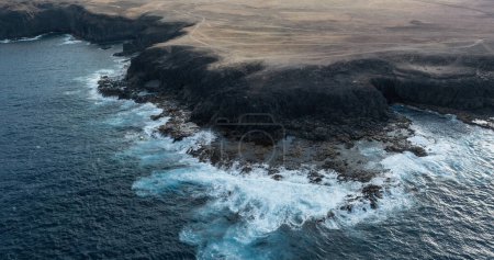 Luftaufnahme einer Wüstenküste mit türkisfarbenen Meereswellen, die auf der Insel Fuerteventura in Spanien gegen die Küste krachen