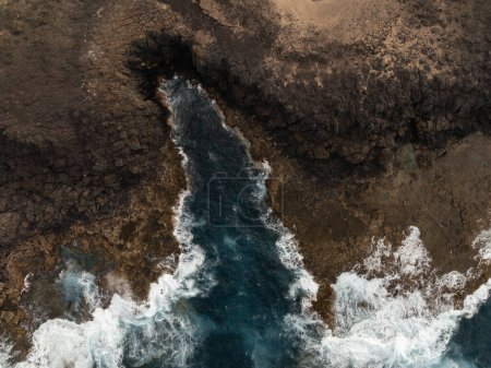 Luftaufnahme eines schmalen Wasserkanals zwischen zerklüftetem Gelände, der auf der Insel Fuerteventura in den Ozean führt