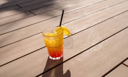 Tropischer Cocktail mit Orangenscheibe auf Holzdeck, Sonnenschein wirft Schatten, erfrischendes Getränk in einem karibischen Inselhotel