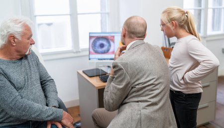 Optometrista revisando el escáner ocular de un paciente mayor en una computadora, su nieta observa con entusiasmo.