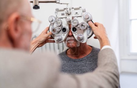 Optometrist adjusting phoropter for senior patient's vision test in clinic