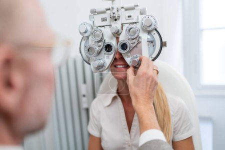 Optometrist adjusting a phoropter for a female patient during an eye test at the ophthalmology clinic. Healthcare and medicine concept