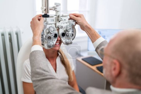 Téléchargez les photos : Optométriste ajustant un phoropter pour un patient lors d'un test oculaire à la clinique d'ophtalmologie. Concept de santé et de médecine - en image libre de droit