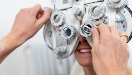 Téléchargez les photos : Gros plan d'un opticien ajustant un phoropter pour une patiente lors d'un test oculaire à la clinique d'ophtalmologie. Concept de santé et de médecine - en image libre de droit